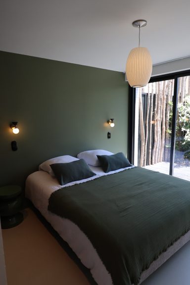 Chambre aux murs vert profond ouverte sur le jardin.