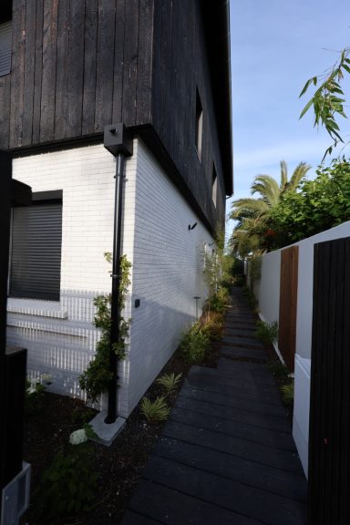 Passage paysager avec pas japonais entre la maison et la clôture en bois.
