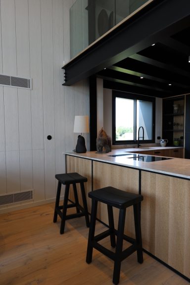 Coin repas de la cuisine avec comptoir en bois et tabourets noirs.
