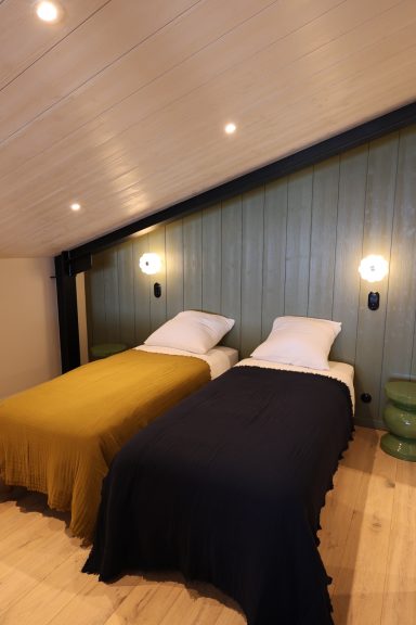 Chambre à deux lits sous plafond rampant avec appliques murales contemporaines.