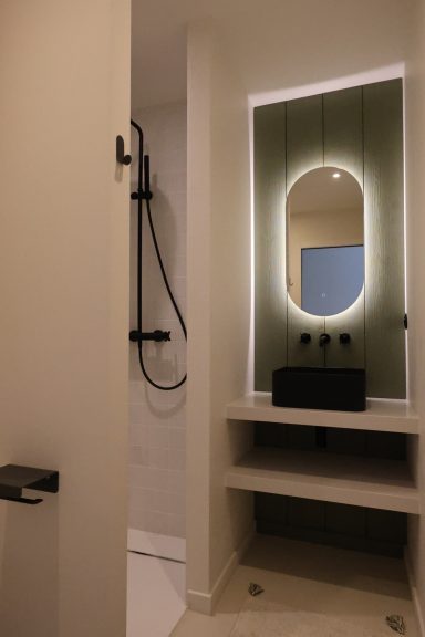 Salle d’eau avec douche noire et miroir rétroéclairé en forme d’arche.