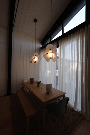 Salle à manger avec table en bois et suspensions sculpturales face aux baies vitrées.