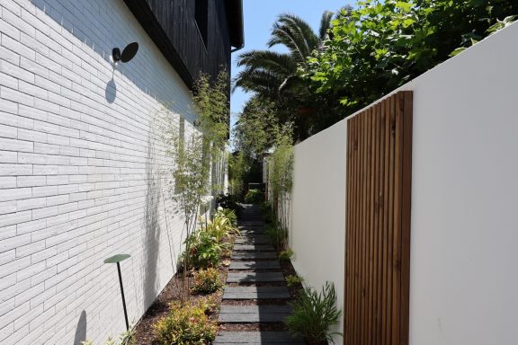 Passage paysager avec pas japonais entre la maison et la clôture en bois.