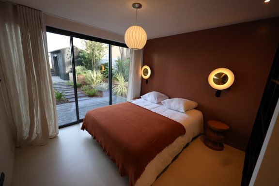 Aménagement d’une chambre aux tons terracotta et éclairage mural circulaire.