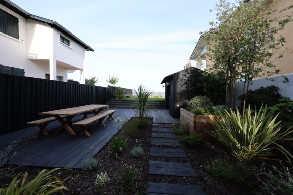 Jardin paysager avec terrasse en bois et cheminement en pas japonais.