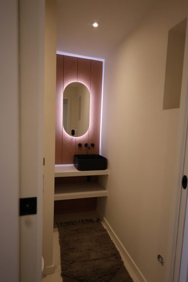 Salle d’eau terracotta avec vasque noire et miroir rétroéclairé.