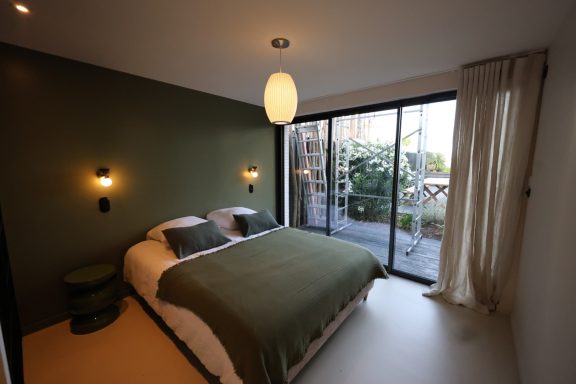 Chambre vert profond avec suspension en fibres et ouverture sur le jardin.