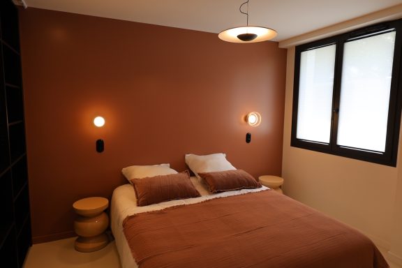 Chambre aux tons terracotta avec éclairage mural et suspension contemporaine.