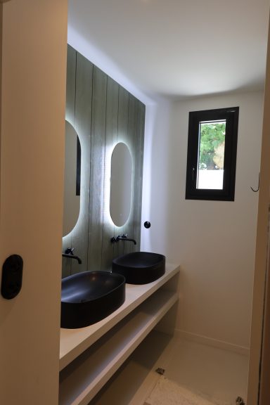 Salle d’eau avec double vasque noire et miroir lumineux.