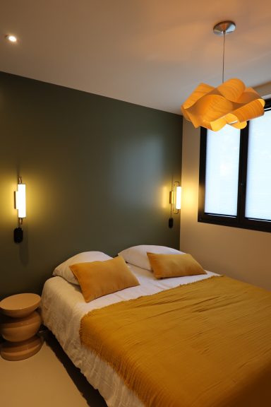 Chambre aux murs vert profond avec linge de lit jaune et éclairage chaleureux.
