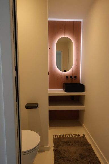 Meuble vasque suspendu et miroir lumineux sur un mur terracotta.