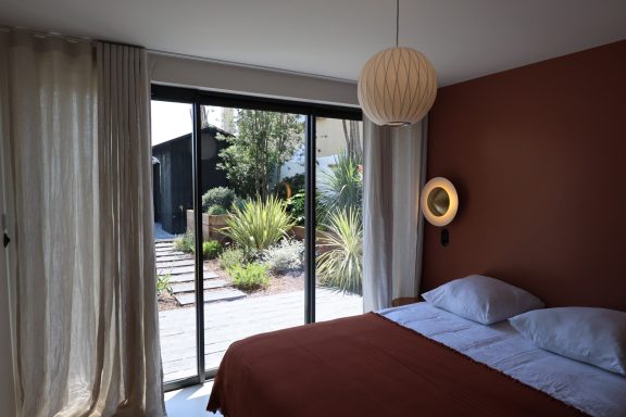 Chambre terracotta avec baie vitrée donnant sur le jardin paysager.