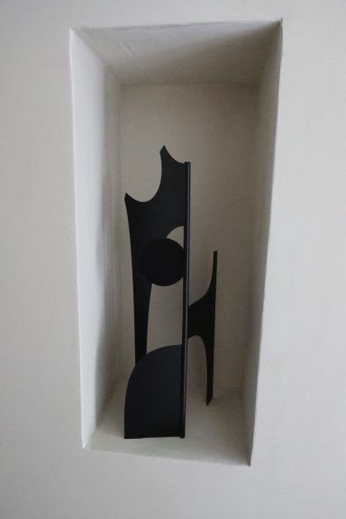 Sculpture noire contemporaine présentée dans une niche murale.